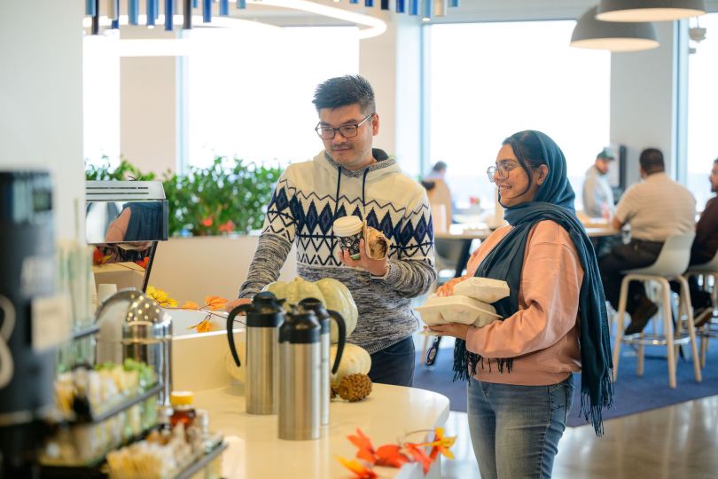 Two employees chat while grabbing coffee and breakfast food inside the company’s office