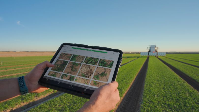 A farmer holds a tablet displaying Carbon Robotics' application while standing in the field