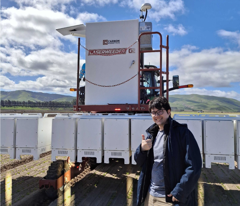 Sho Anegawa takes a photo next to Carbon Robotics' LaserWeeder technology in the field.