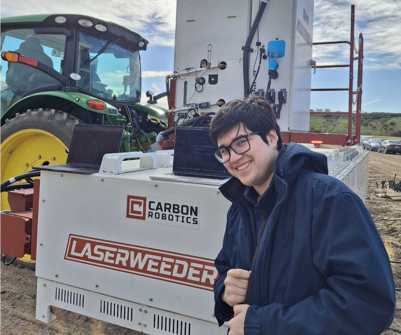 Sho Anegawa takes a photo next to Carbon Robotics' LaserWeeder technology in the field.