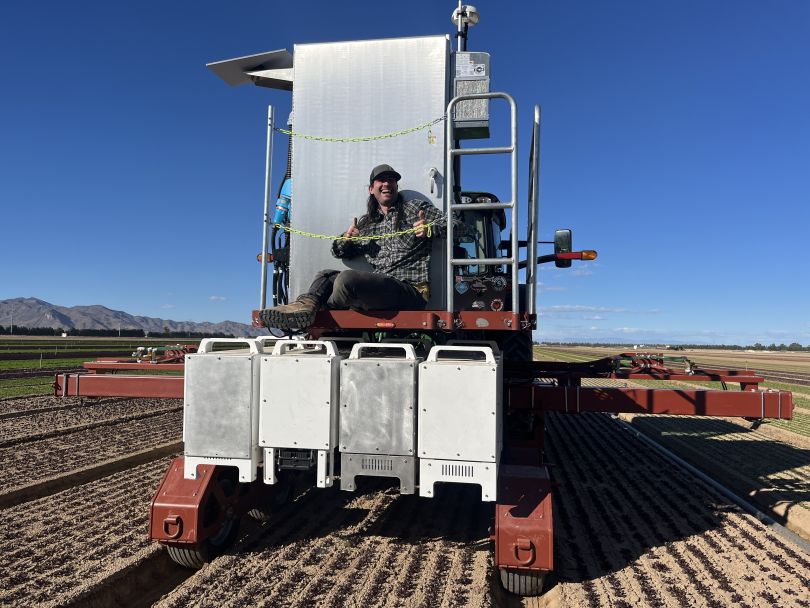 A Carbon Robotics team member sits on one of the company’s machines while working in a field