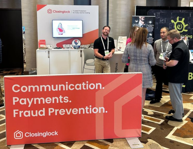 A Closinglock employee poses for a photo in front of a Closinglock booth during a convention next to colleagues chatting together.&nbsp;
