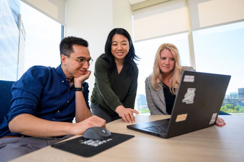 Three Cox Enterprises employees view information on a laptop screen while working together inside one of the company's offices