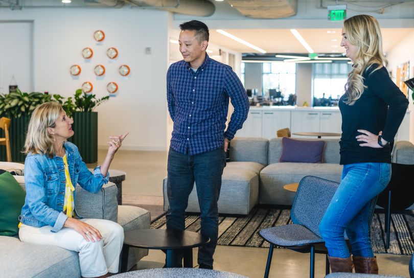 Three Udemy team members, some standing and some sitting, in discussion