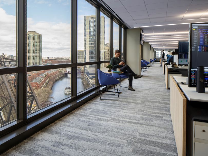 A Gelber Group, LLC. employee sits on a chair while scrolling through his phone next to a window overlooking the Chicago River in the firm’s office