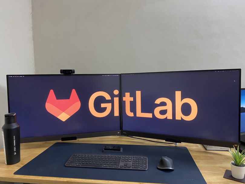 The GitLab logo displayed across two computer monitors in an employee’s home office