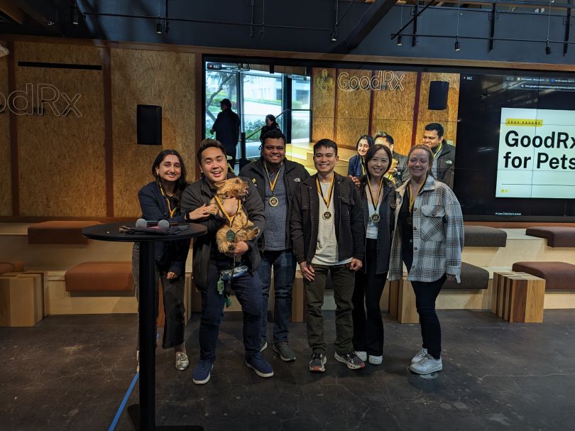 Several GoodRx team members, including one holding a dog, pose for a  group photo during a company event.