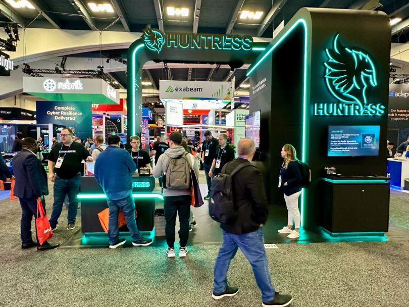 People gather around a booth showcasing Huntress’s products at a tech industry conference