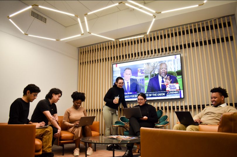 NBCUniversal team members in a meeting sitting on couches and lounge chairs, with MSNBC channel on a TV on the wall.&nbsp;