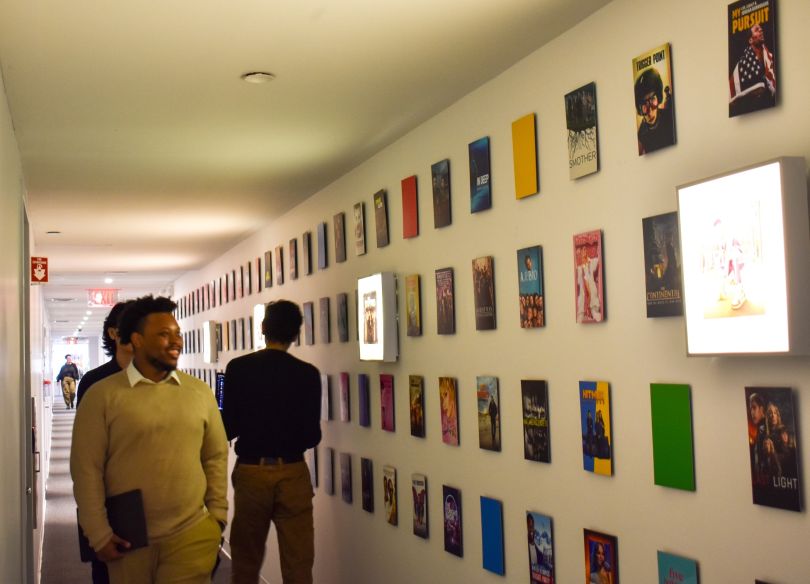 NBCUniversal team members walk through office hallway lined with artwork promoting the brand’s TV series.&nbsp;
