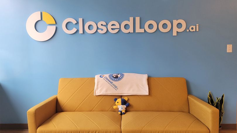 A yellow couch against a blue wall featuring ClosedLoop’s logo.&nbsp;