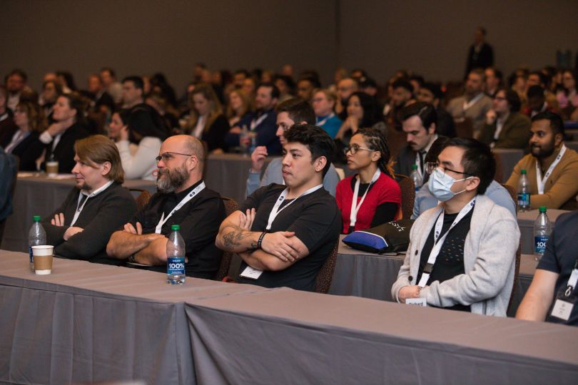  A group of Level Access employees sit and listen to a speaker in a large lecture hall&nbsp;