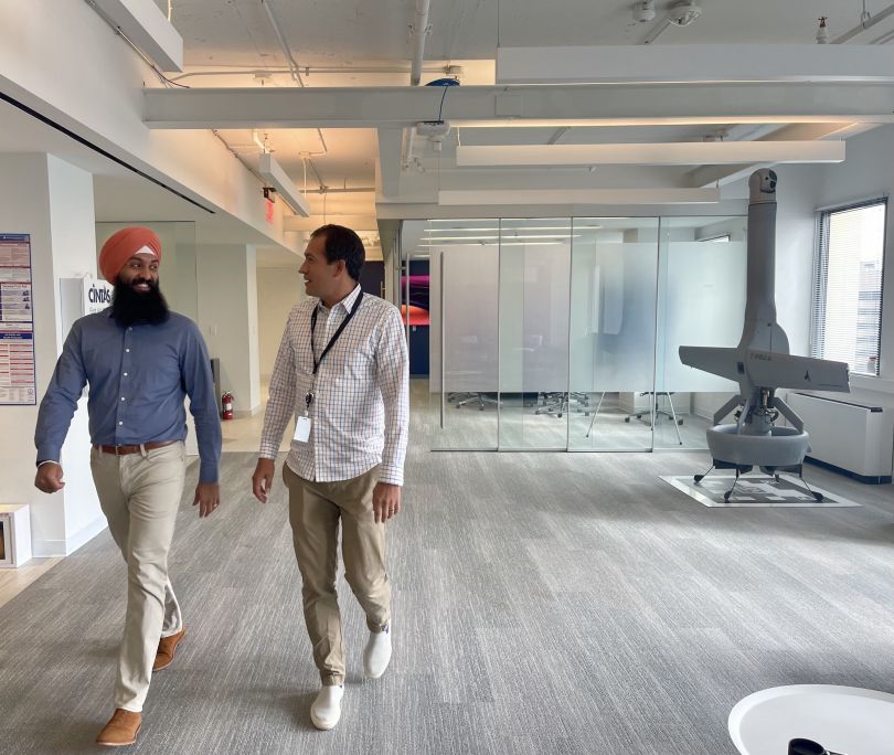 Two Shield AI employees walk down a hallway near a model of a drone.&nbsp;