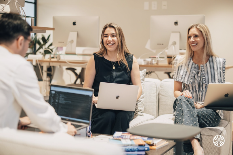 Two Mirakl team members laugh while working on a project with their colleague in the office