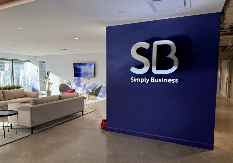 A lounge space in Simply Business’ Boston office featuring couches and a wall imprinted with the company’s logo