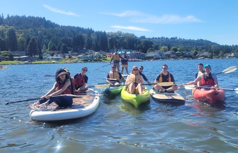 A group of Clean Power Research employees post for a photo while floating on paddleboards and in kayaks. 