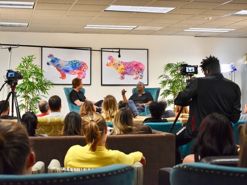 A fireside chat event with two leaders in armchairs talking in front of an audience of team members and cameras.&nbsp;