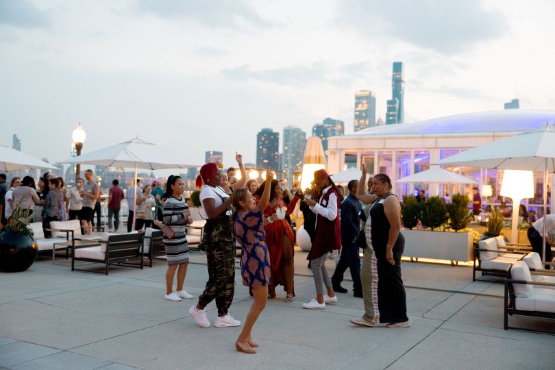 OppFi team members cheer in outdoor rooftop setting with Chicago skyline in the background at dusk during a Thrive Where You Work Week event.&nbsp;