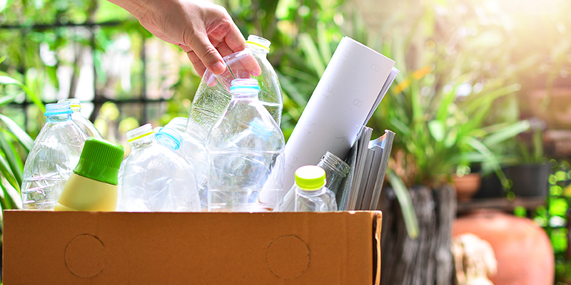 A person placing a plastic bottle into a box of recycled goods.
