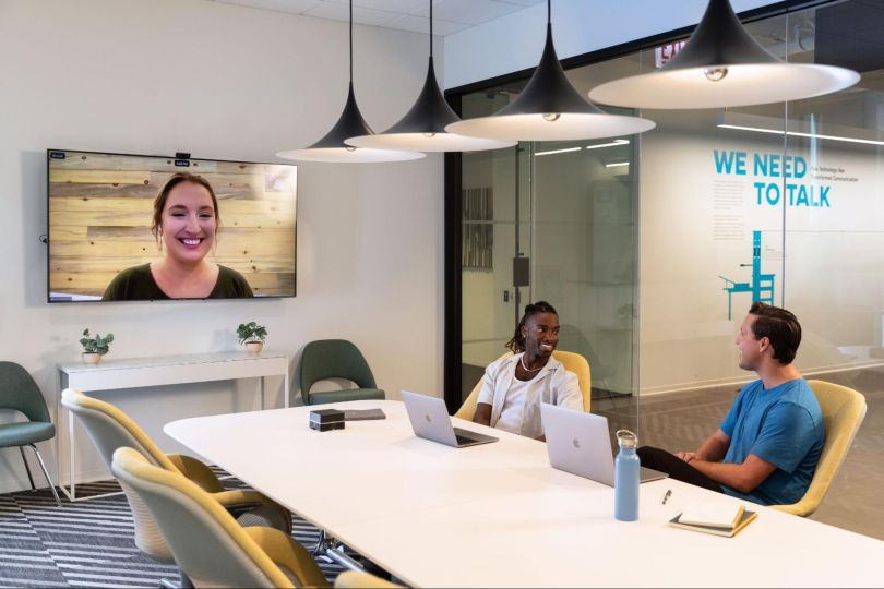 Three Sprout Social employees having a meeting in the office with one person joining remotely.