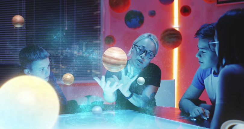 A woman motions toward holograms of planets while children watch.&nbsp;