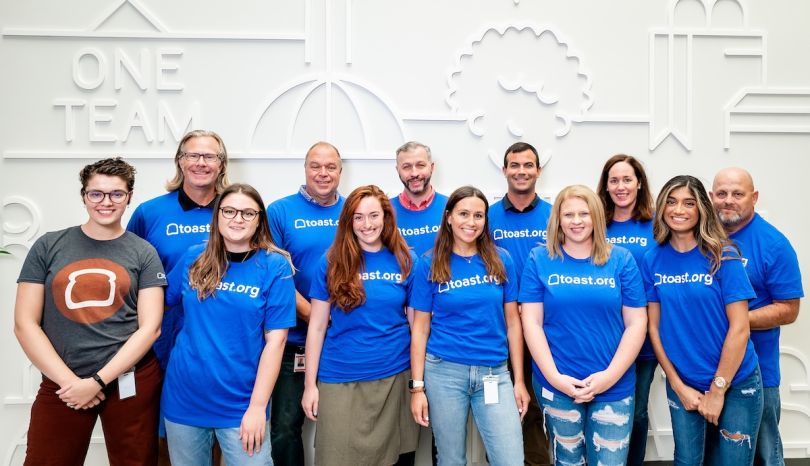Team members from Toast pose for a group photo in matching company t-shirts.&nbsp;