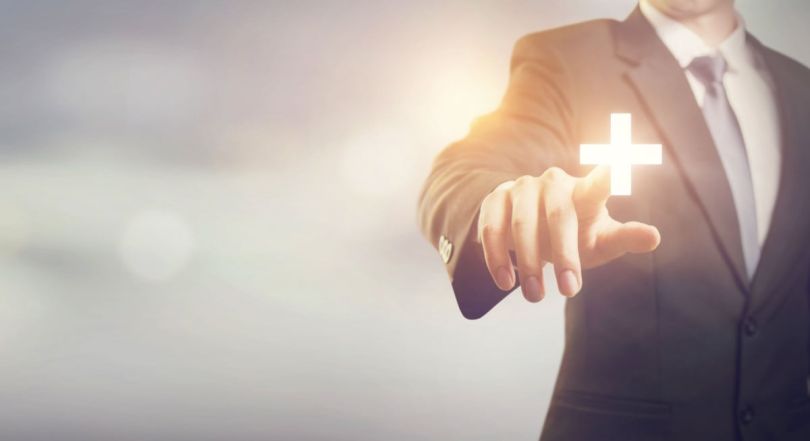 A professional reaching out toward a glowing plus sign at the fingertips.