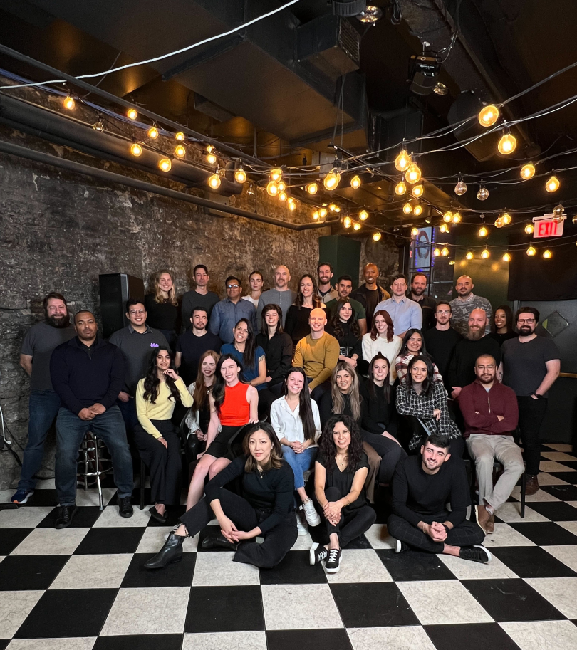 team photo of pinata in nashville in an indoor space with string lights hanging overhead, exposed brick walls and black and white tile floors