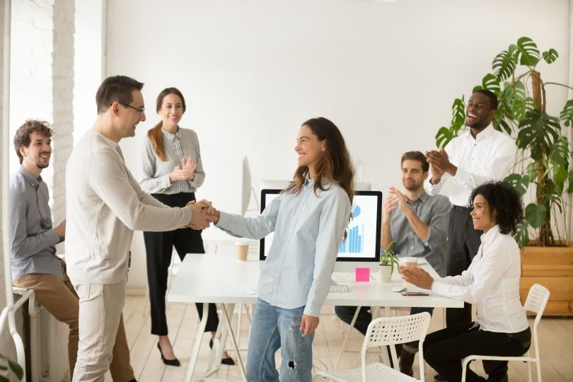 A woman and man shake hands in an office setting.