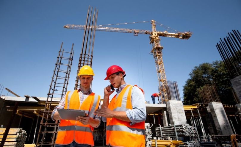 Two construction workers chat on the phone and look at iPad