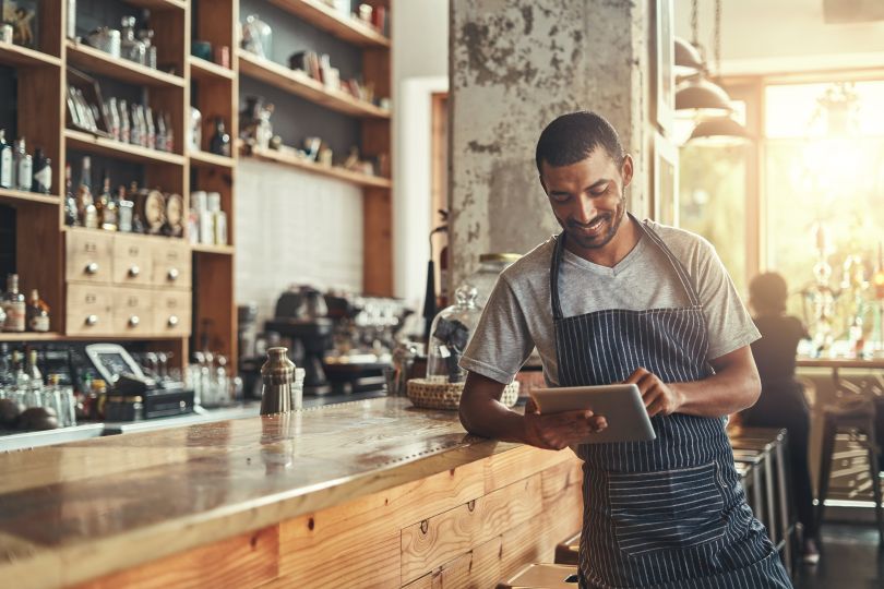 A restaurant professional leans against the bar and uses an iPad. 