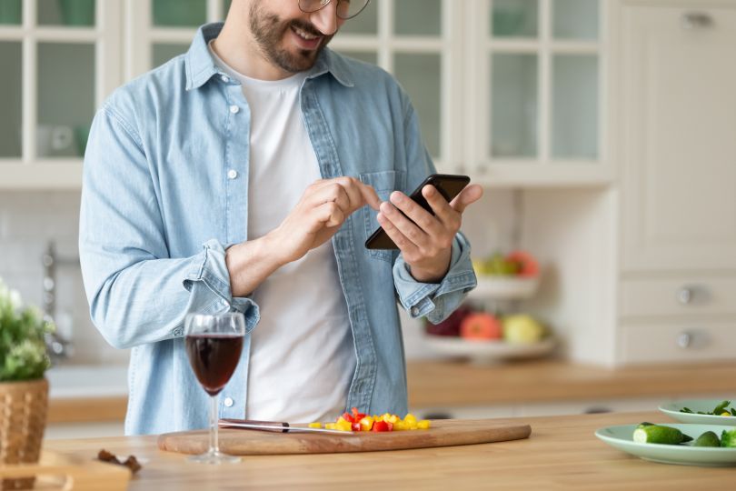 A man with a glass of wine ordering something on his phone.