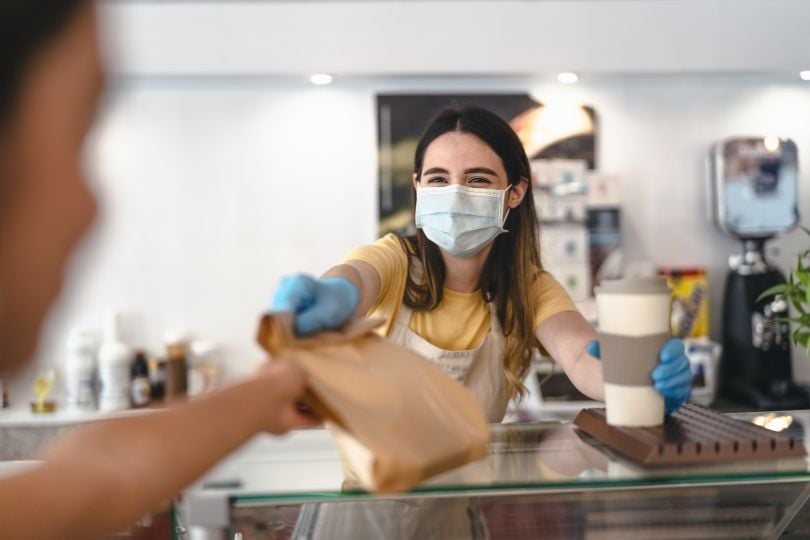 A frontline worker hands a customer a bag and drink.
