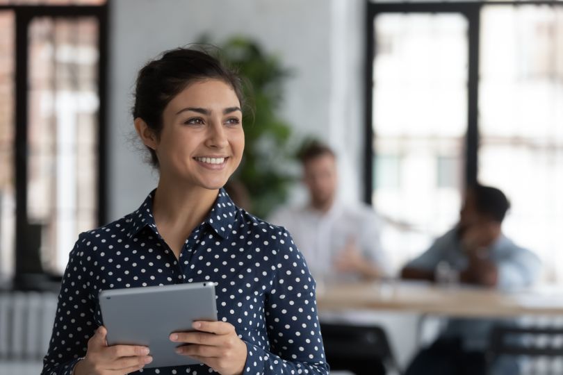 A young woman holds an iPad and smiles.  