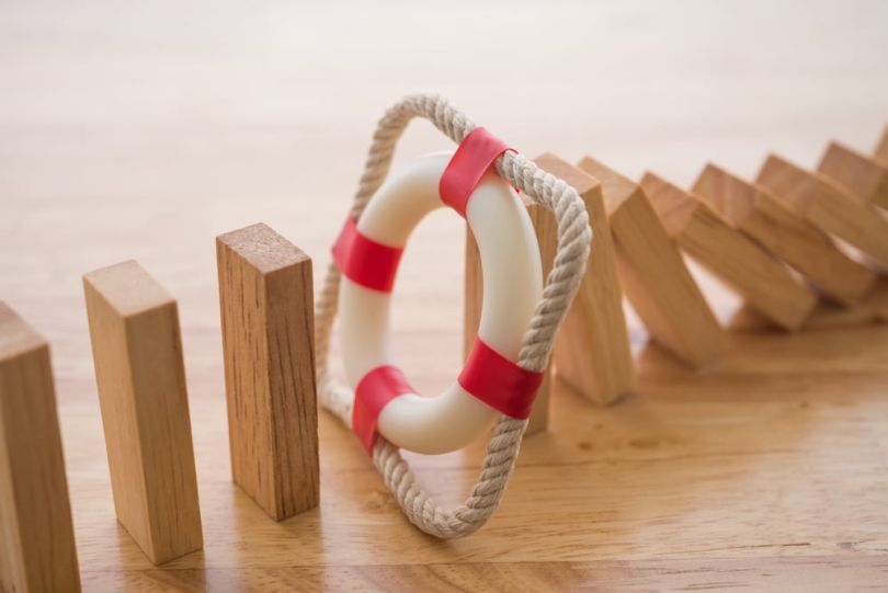 Jenga blocks fall in a line, stopping at a counter-weighted life preserver.&nbsp;