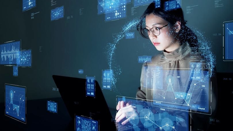 A woman sits at a computer terminal while abstractions of data swirl around her