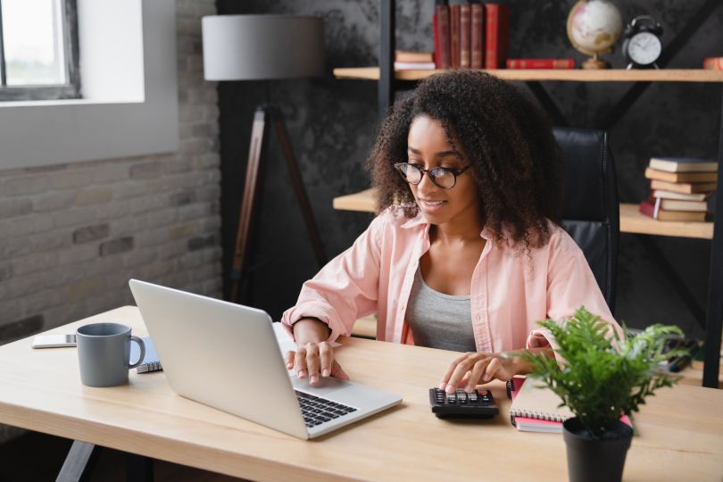 A woman working on her laptop and using a calculator. 