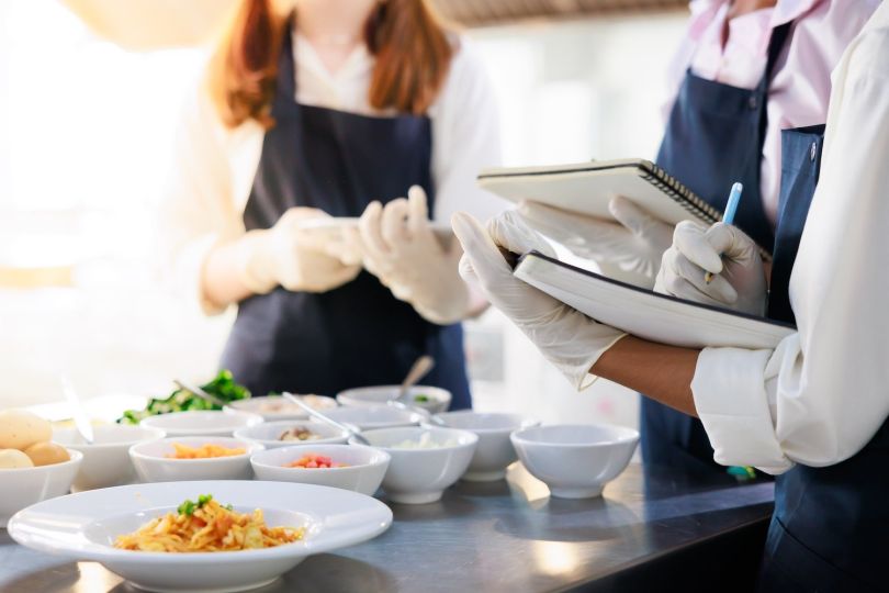 Three chefs writing recipe in a notebook with food plated on a table in front of them