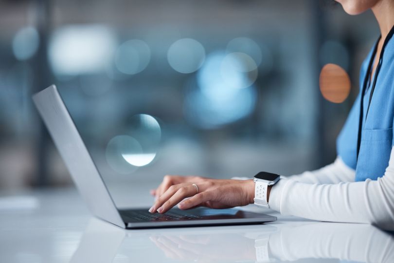 A medical professional types on a laptop.