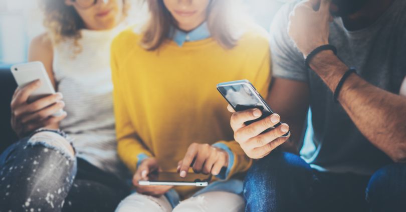 Three people look at two smartphones and a tablet