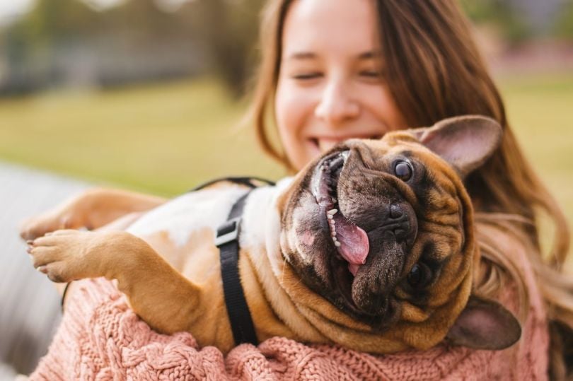 A woman holds a dog in her arms as the dog sticks its tongue out.