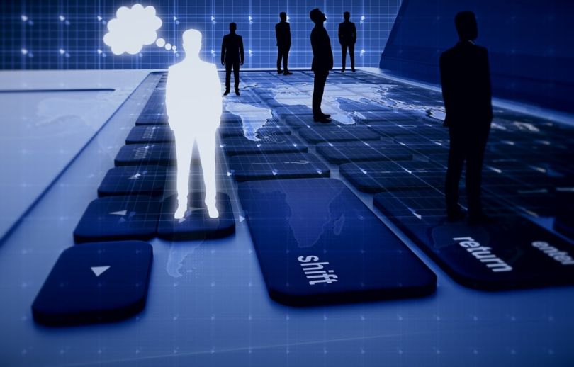 Silhouettes of business people stand on top of a computer keyboard.