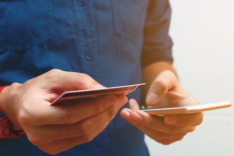 A man holds both a debit card and his phone while consulting an app.