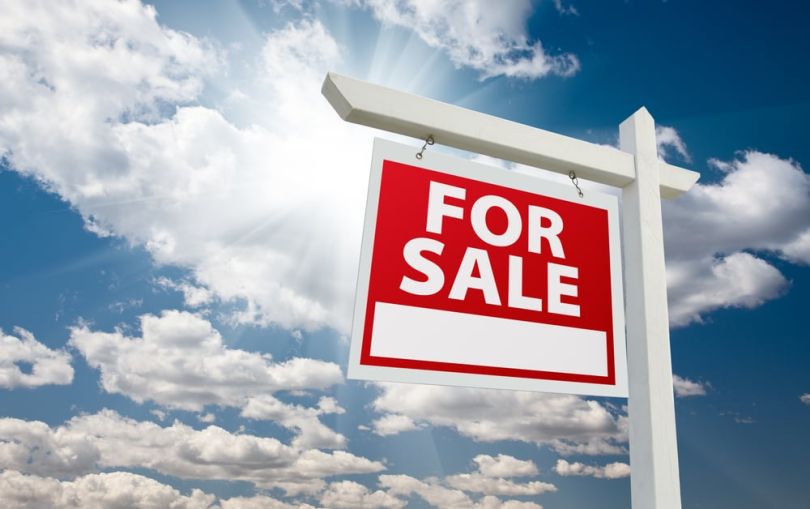 For sale sign over clouds and blue sky.