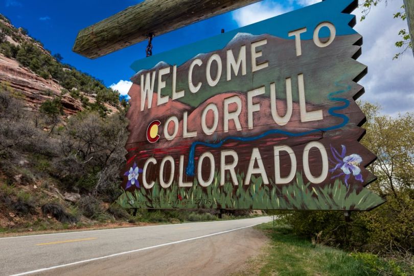 A Welcome to Colorado road sign with mountain landscape behind it.