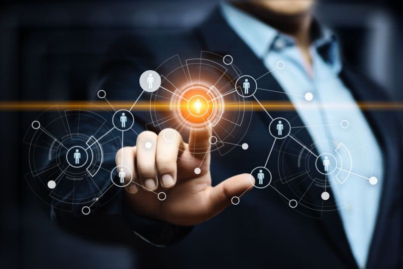 A person’s finger pointing at a virtual network of human icons surrounding a central figure.