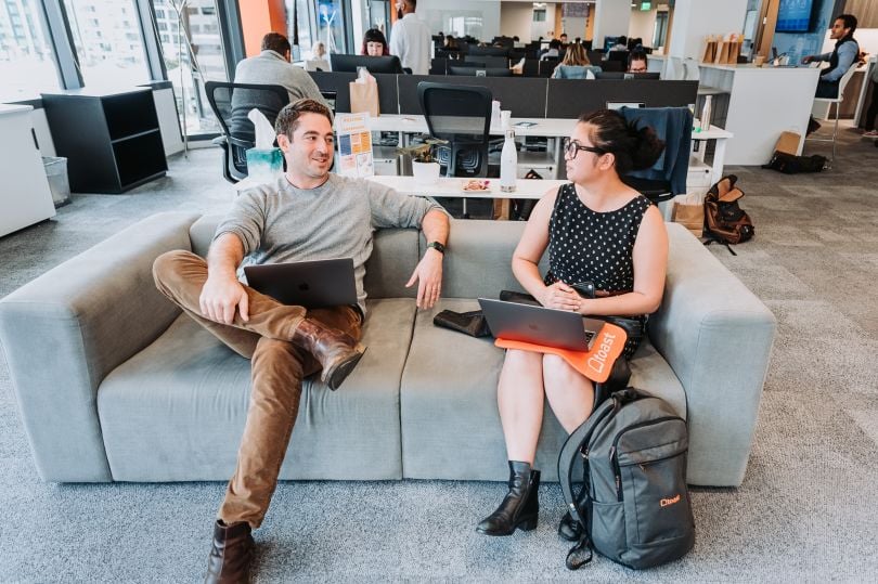 Toast employees sit on a grey couch and chat over their laptops at the Toast offices.