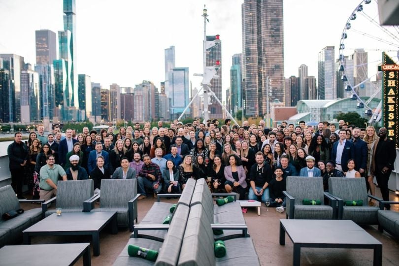 A large group of Vouch professionals pose for a group photo in front of the Chicago skyline.&nbsp;